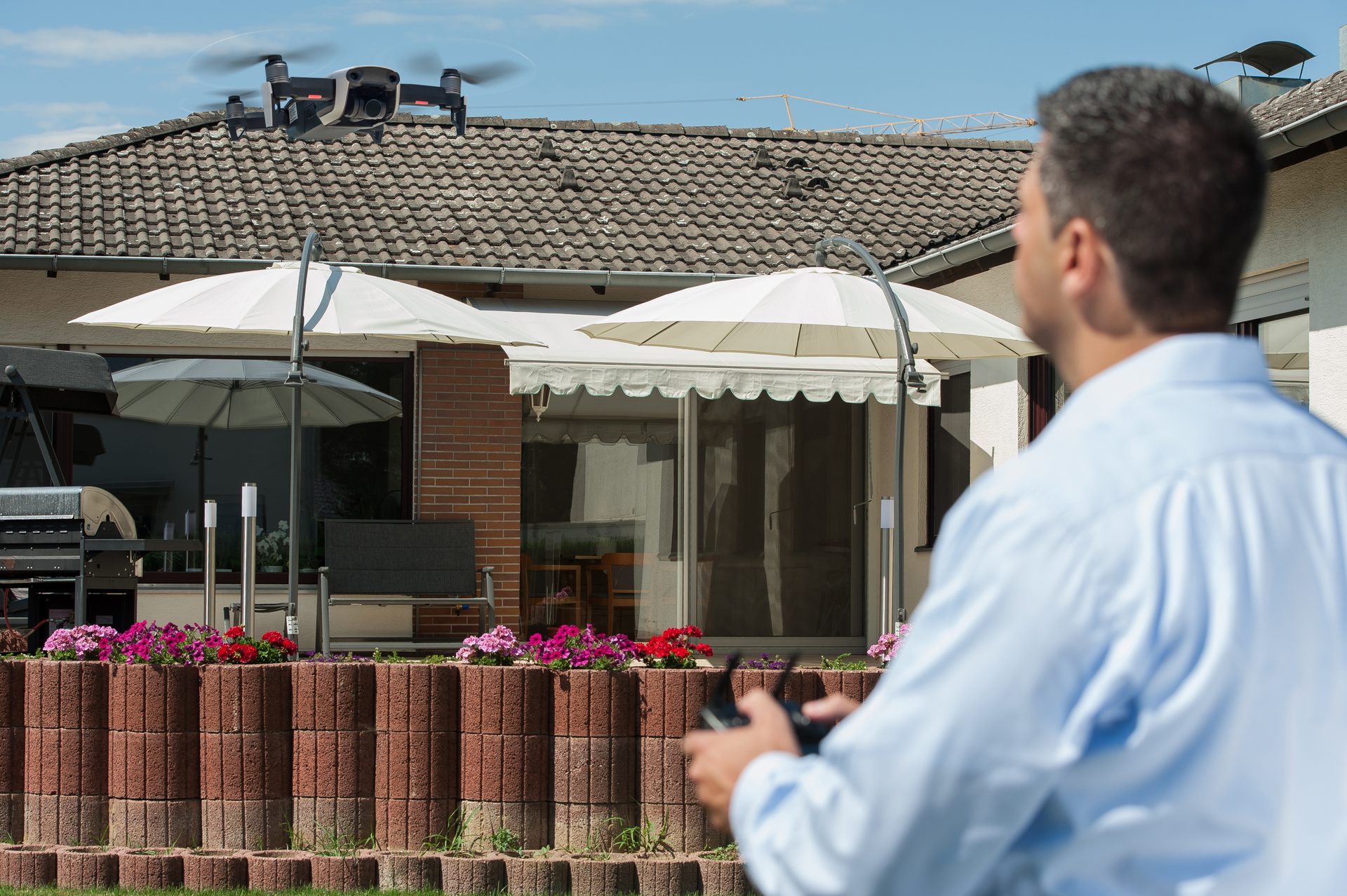 Makler steuert eine Drohne über einem Einfamilienhaus mit Garten für die Luftaufnahme
