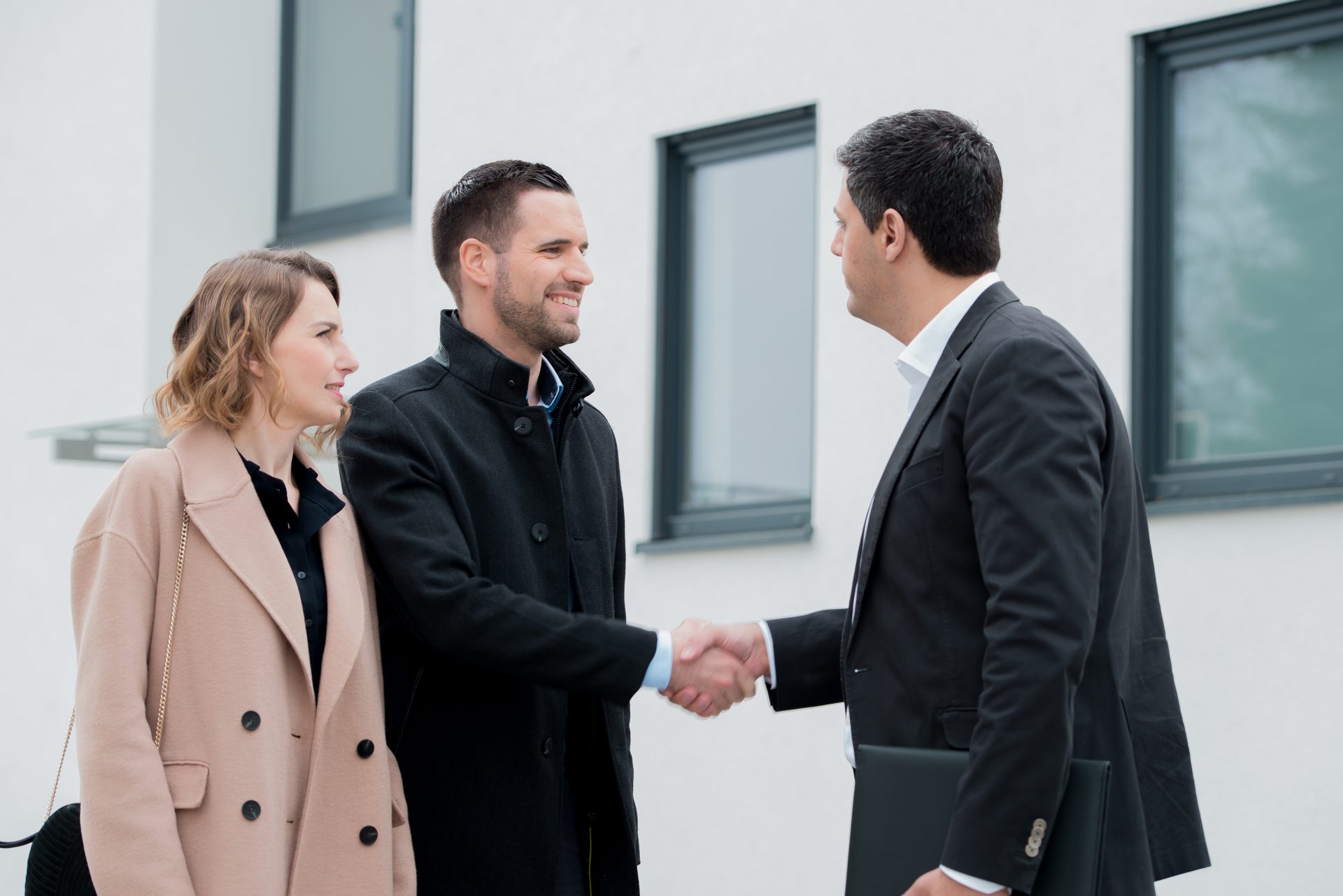 Handschlag zwischen Makler und Käuferpaar vor einem Wohnhaus